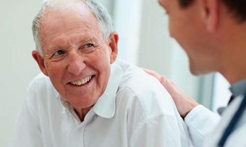 Doctor with a hand on older smiling man discussing prostate cancer