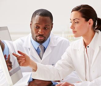 Man and woman in lab coats looking at computer screen
